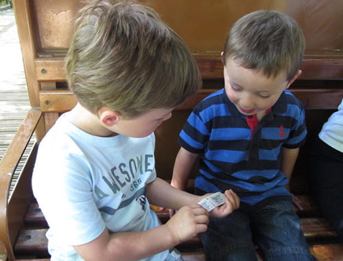 Two young children sitting beside each other on a train. One is showing something to the other.